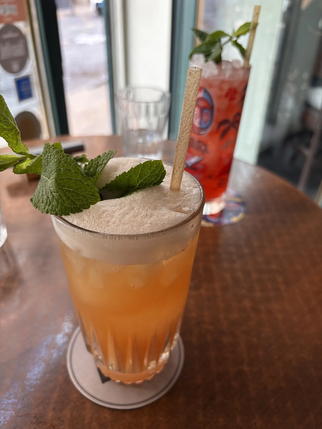 A frothy orange cocktail with a mint sprig and a straw in a tall glass