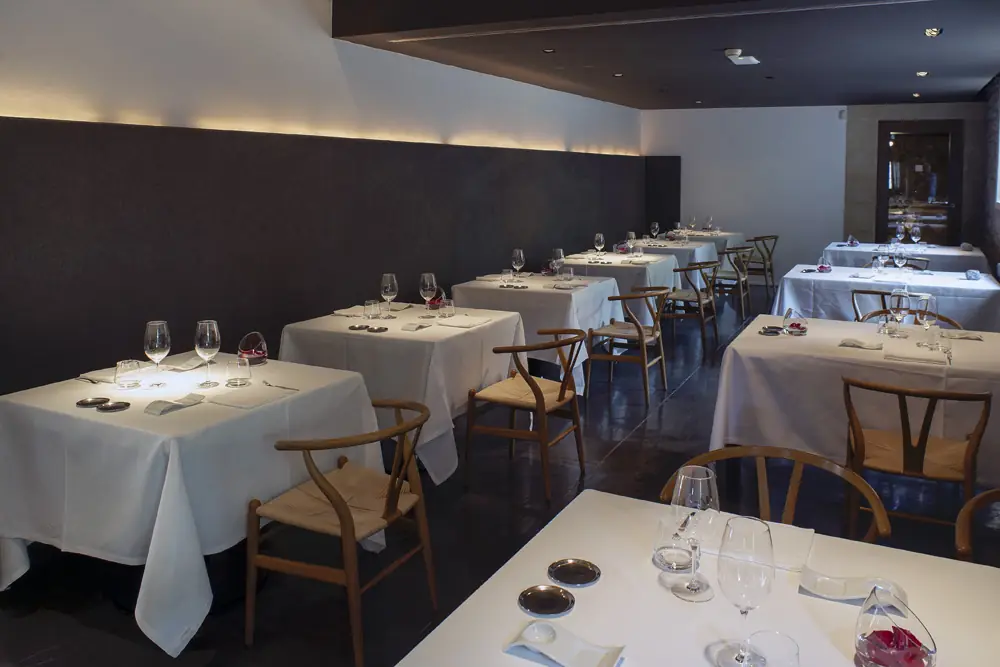 Elegant dining room with white tablecloths, wine glasses, and wishbone chairs.