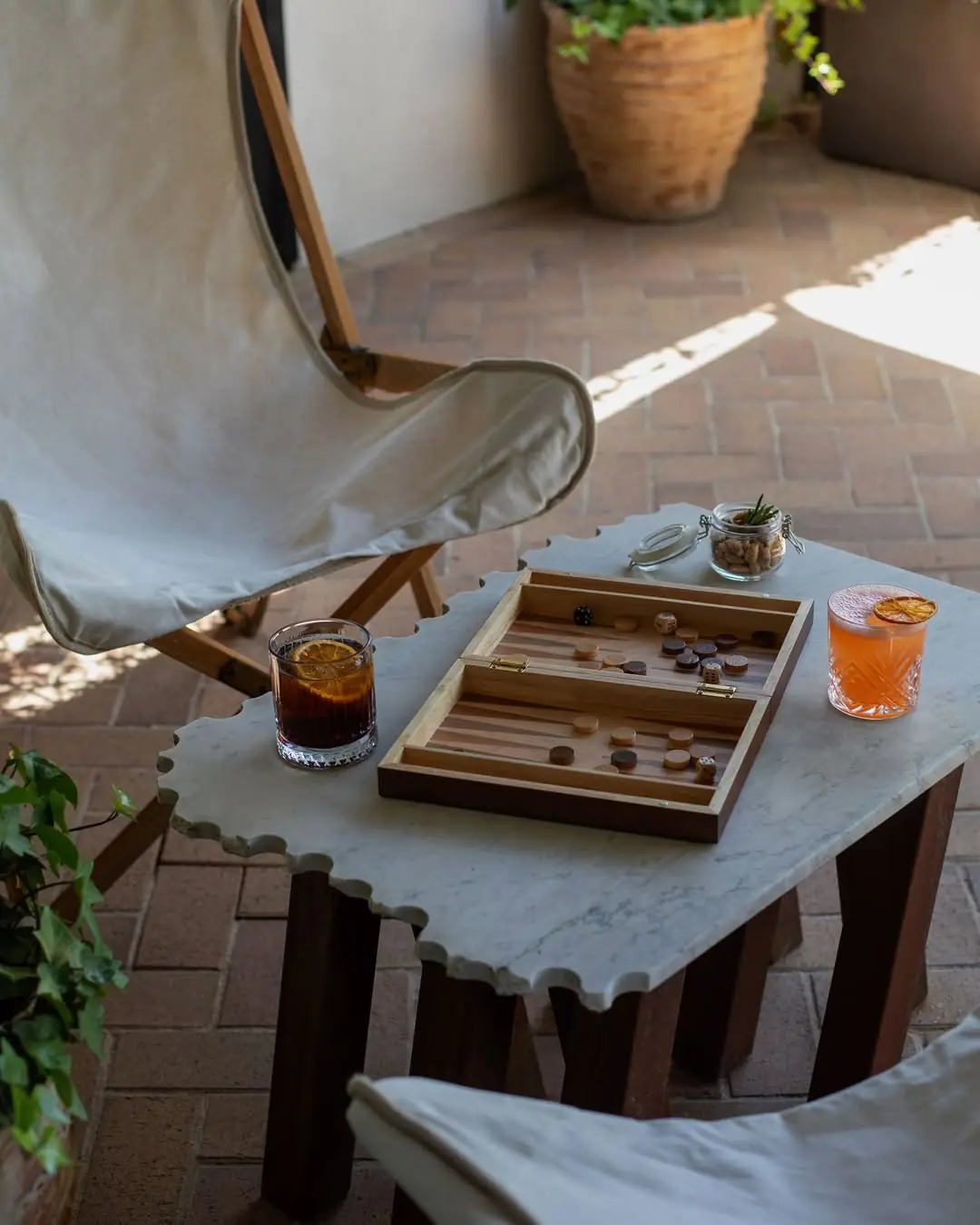 Two served cocktails with orange garnish next to a backgammon set on an outdoor table