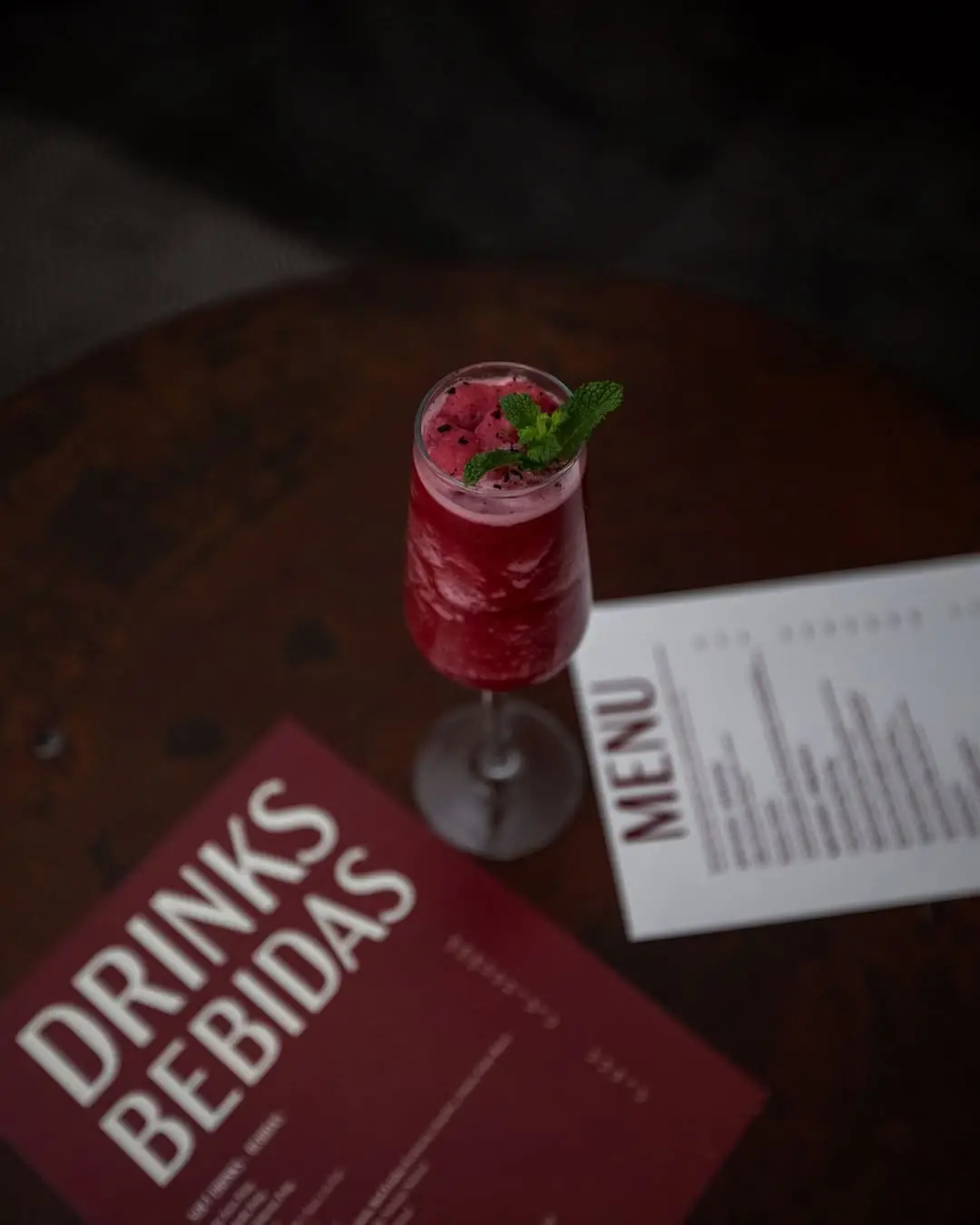 A pink cocktail garnished with mint on a table beside drink and food menus