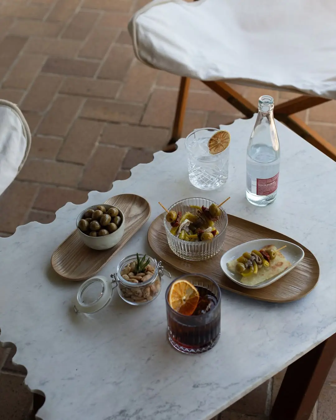 A spread of olives, snacks, and two cocktails on a marble table