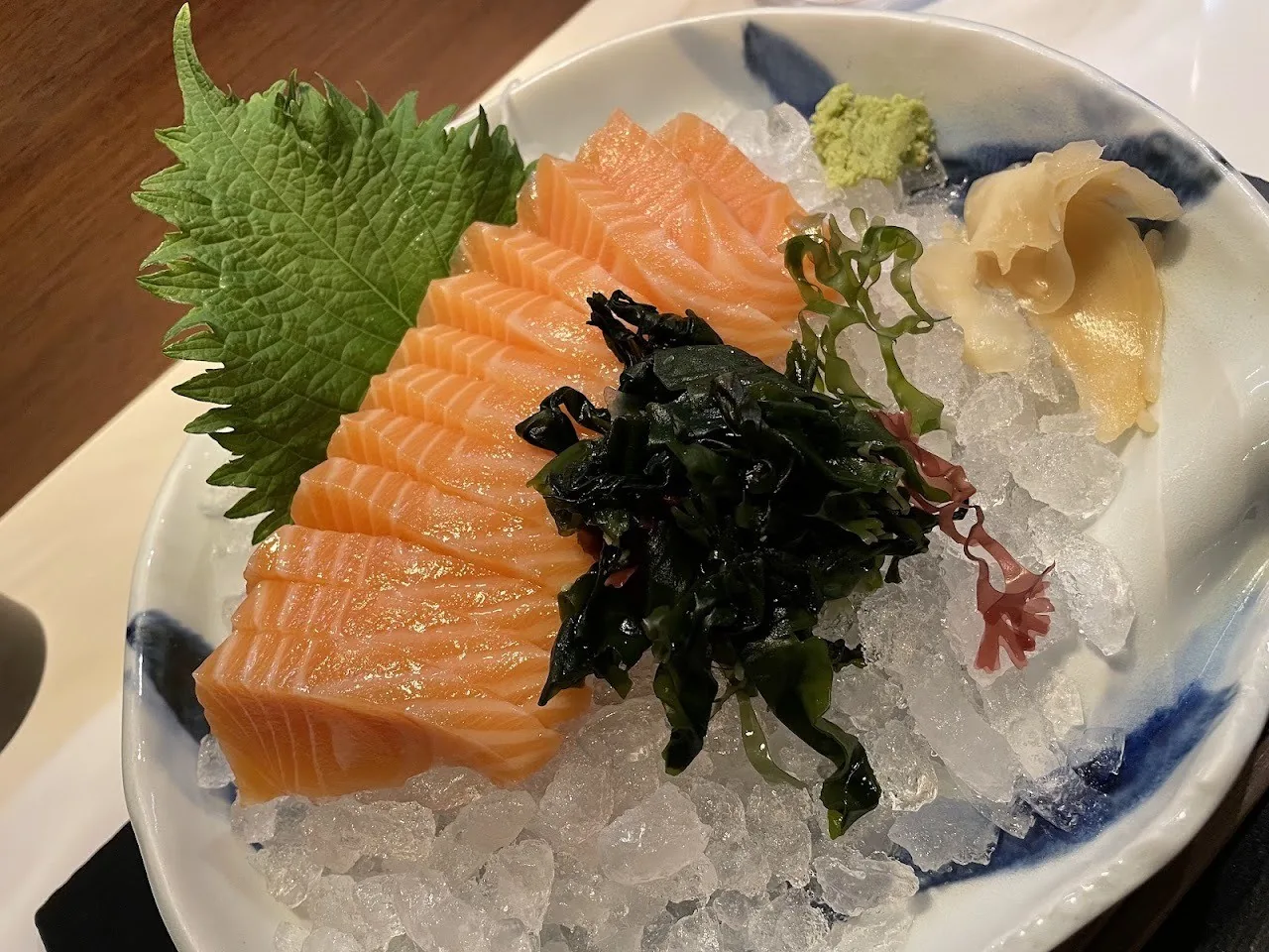 Salmon sashimi with seaweed on ice on a blue and white plate