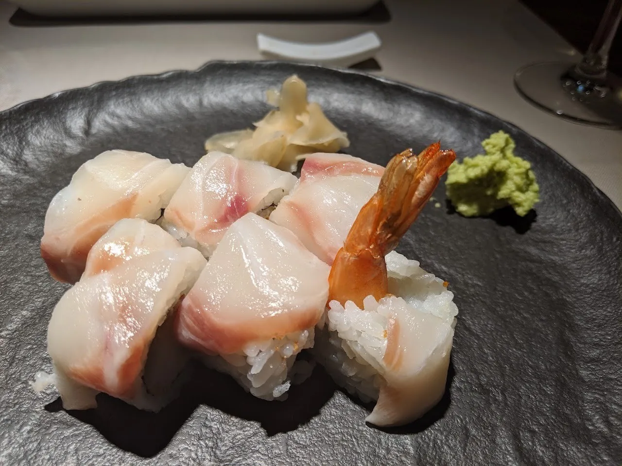 Pieces of white fish nigiri and a prawn on a dark plate with wasabi