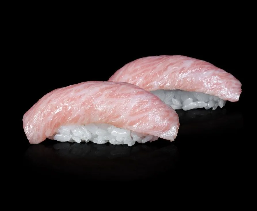 Two pieces of pale pink tuna nigiri on a black background