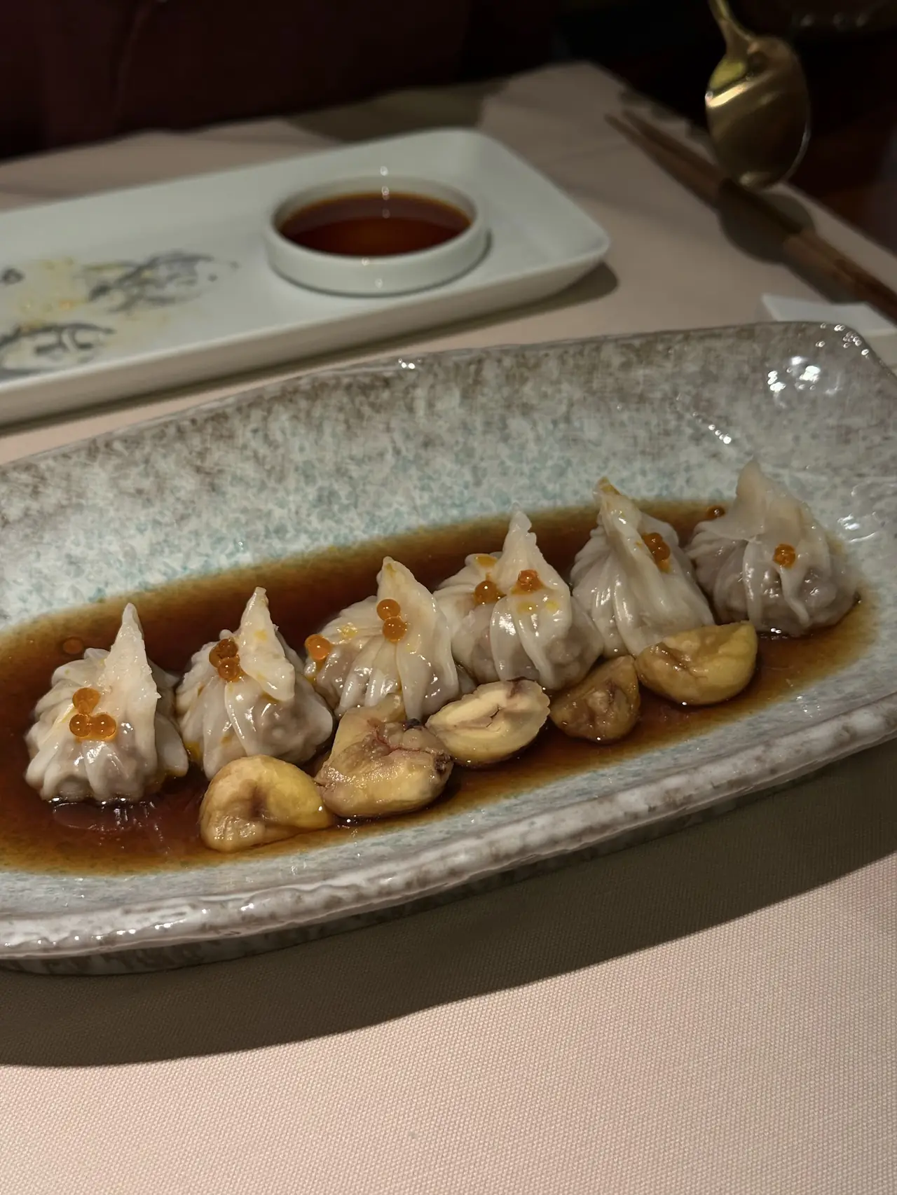 Steamed dumplings topped with orange roe, plated in soy broth with mushroom pieces