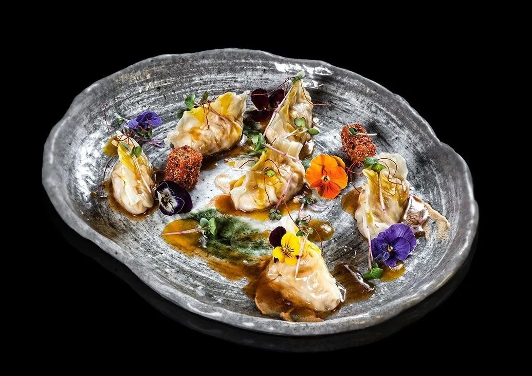 A grey ceramic plate of small seafood dishes with edible flowers on a black background