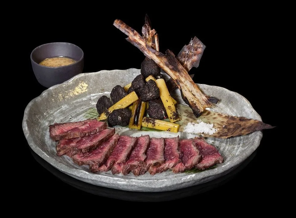 Sliced rare beef and grilled skewered ribs on a grey plate