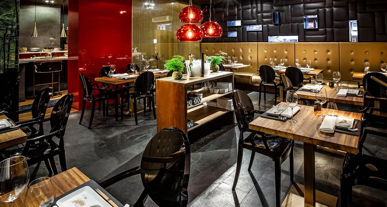 Dining room with red pendant lamps, dark leather wall panels, and tables set with wine glasses