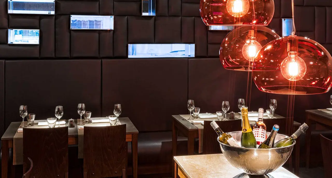 Dining room with dark banquette seating, red pendant lamps, and a silver bowl of chilled wine bottles