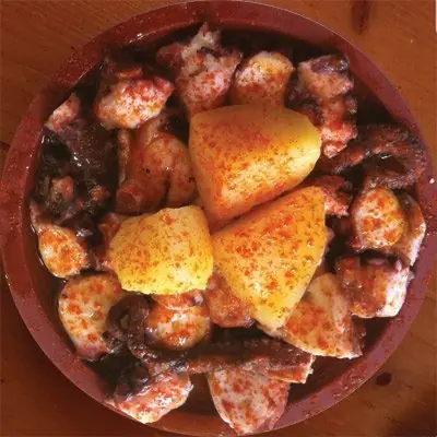 Galician-style octopus (pulpo a feira) with paprika, olive oil, and boiled potato wedges on a wooden plate, A Gudiña