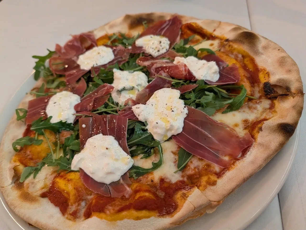 A pizza topped with cured ham, rocket and dollops of white cheese on a plate