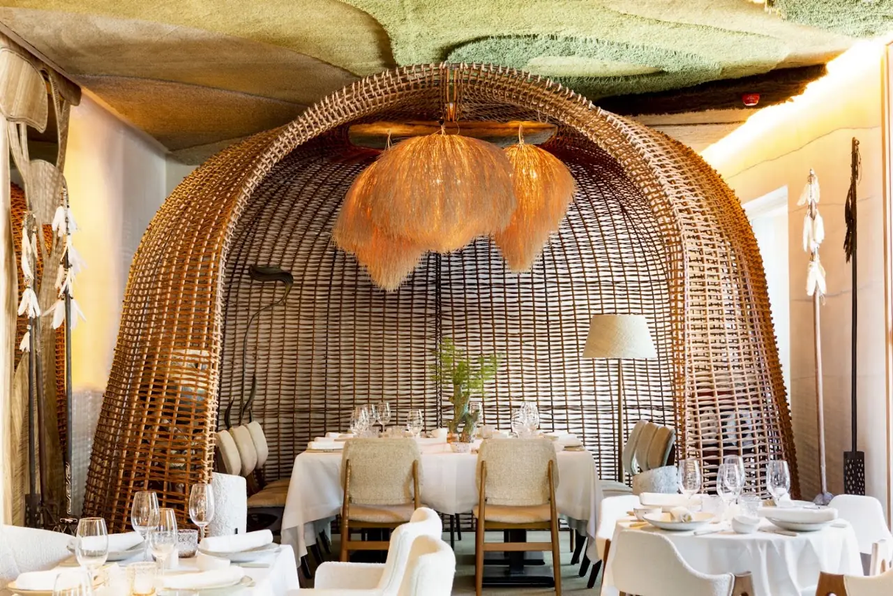Restaurant dining room with woven wicker pendant lamps over white-linen tables.
