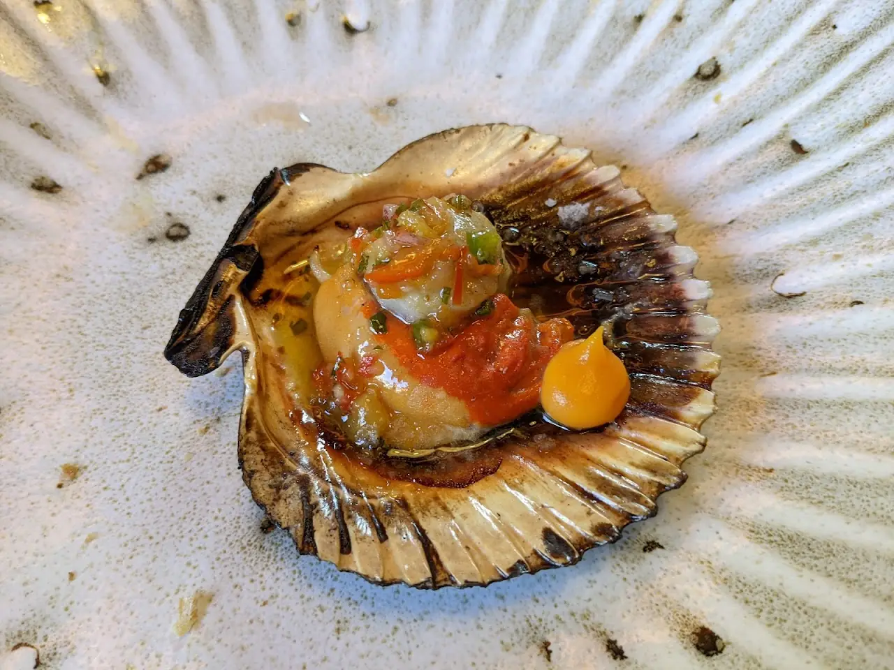 A single scallop in its shell topped with diced tomato and herbs.