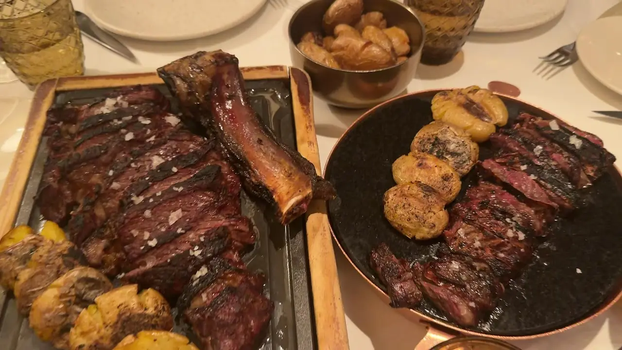 Two cuts of grilled steak with roasted potatoes served on a metal board.
