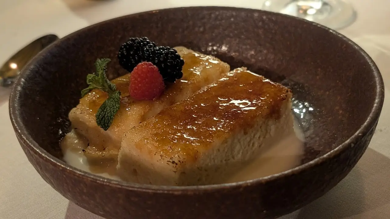 A caramelized dessert topped with fresh berries and mint in a dark bowl.