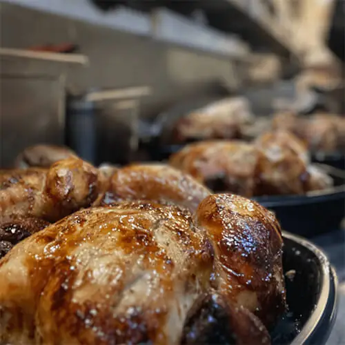 Glossy roast chickens (pollo a la brasa) in pans on a grill