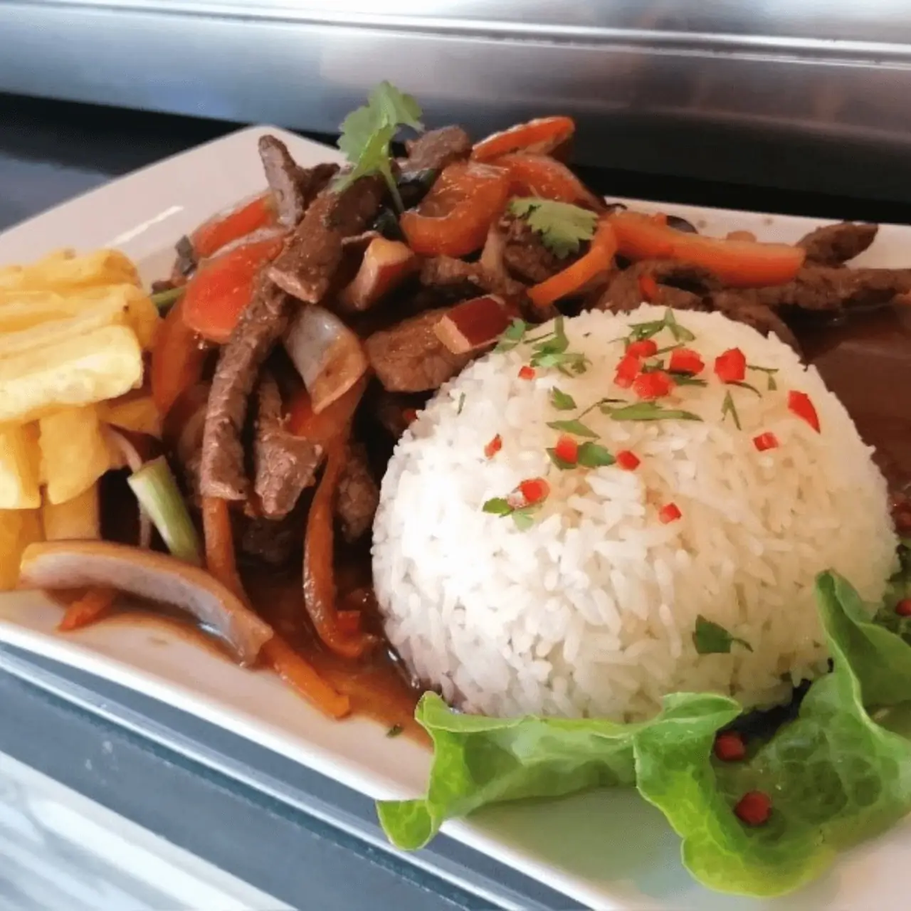 Lomo saltado of beef strips and peppers with white rice and fries on a white plate