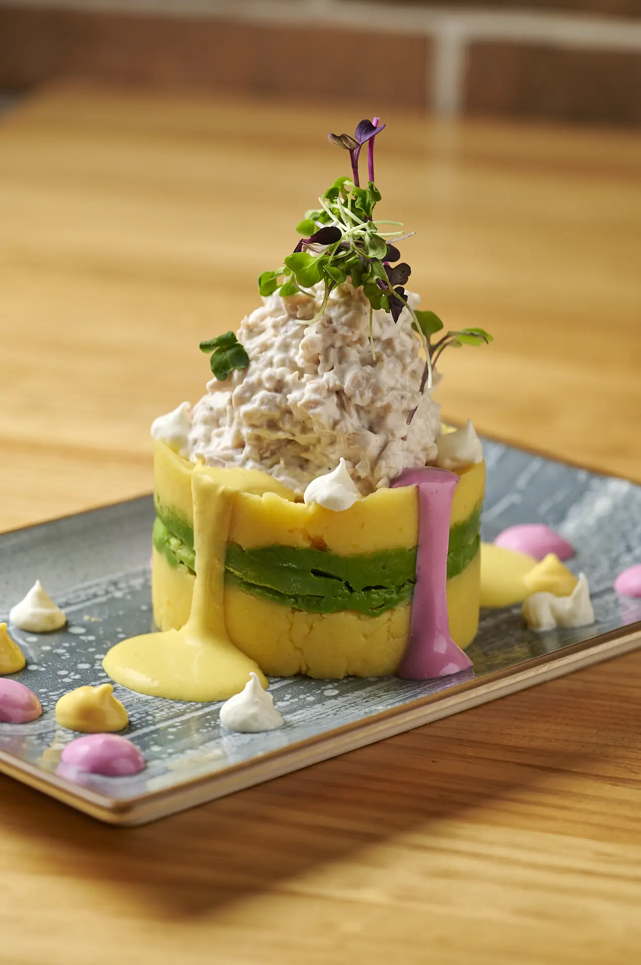 A layered potato tower topped with a creamy filling and microgreens