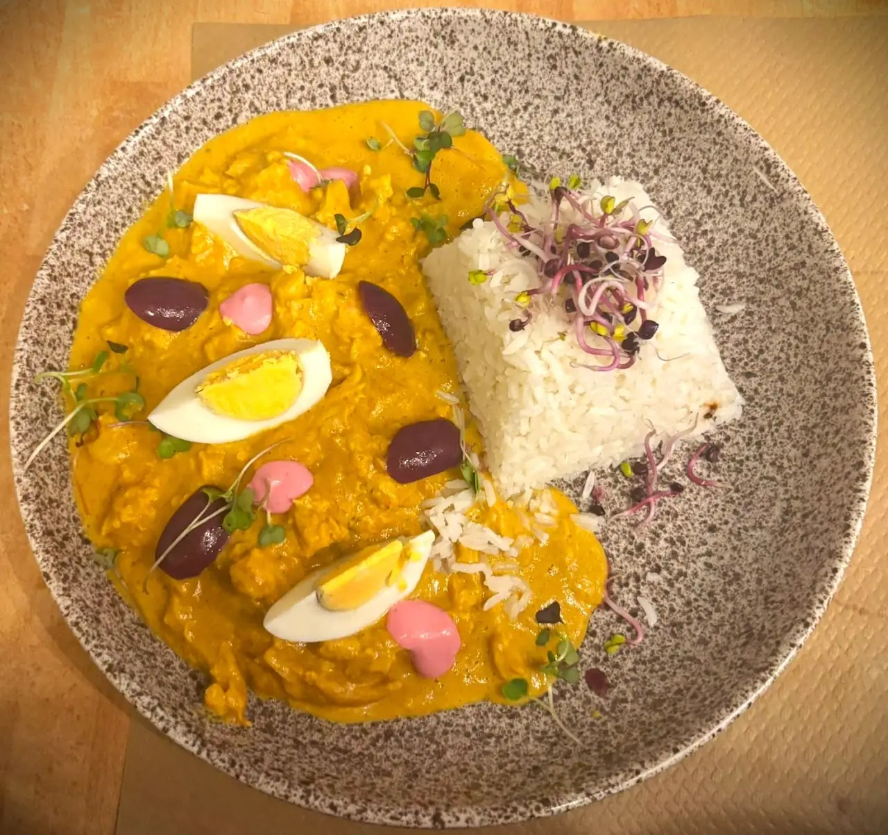 A creamy yellow stew with boiled egg halves and olives, served with a block of rice