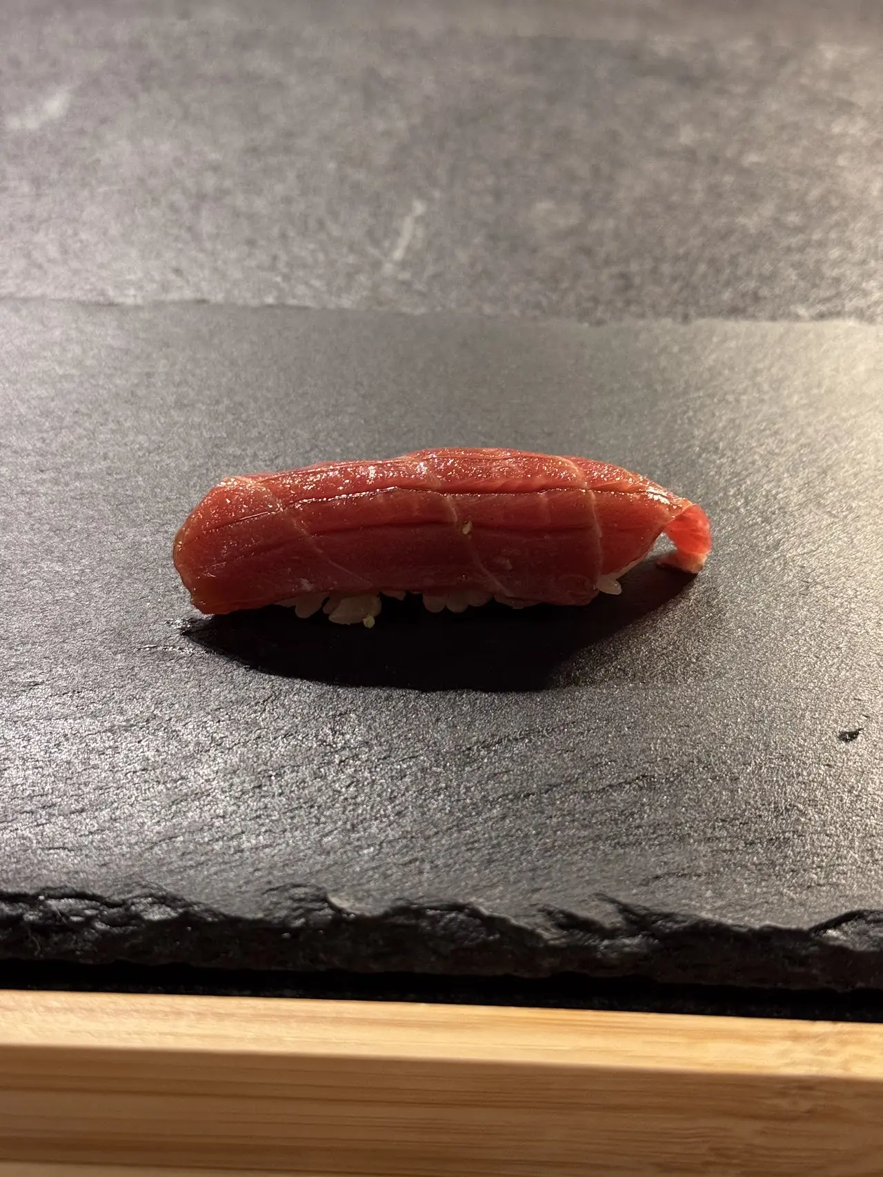 A single piece of tuna nigiri on a dark slate board.