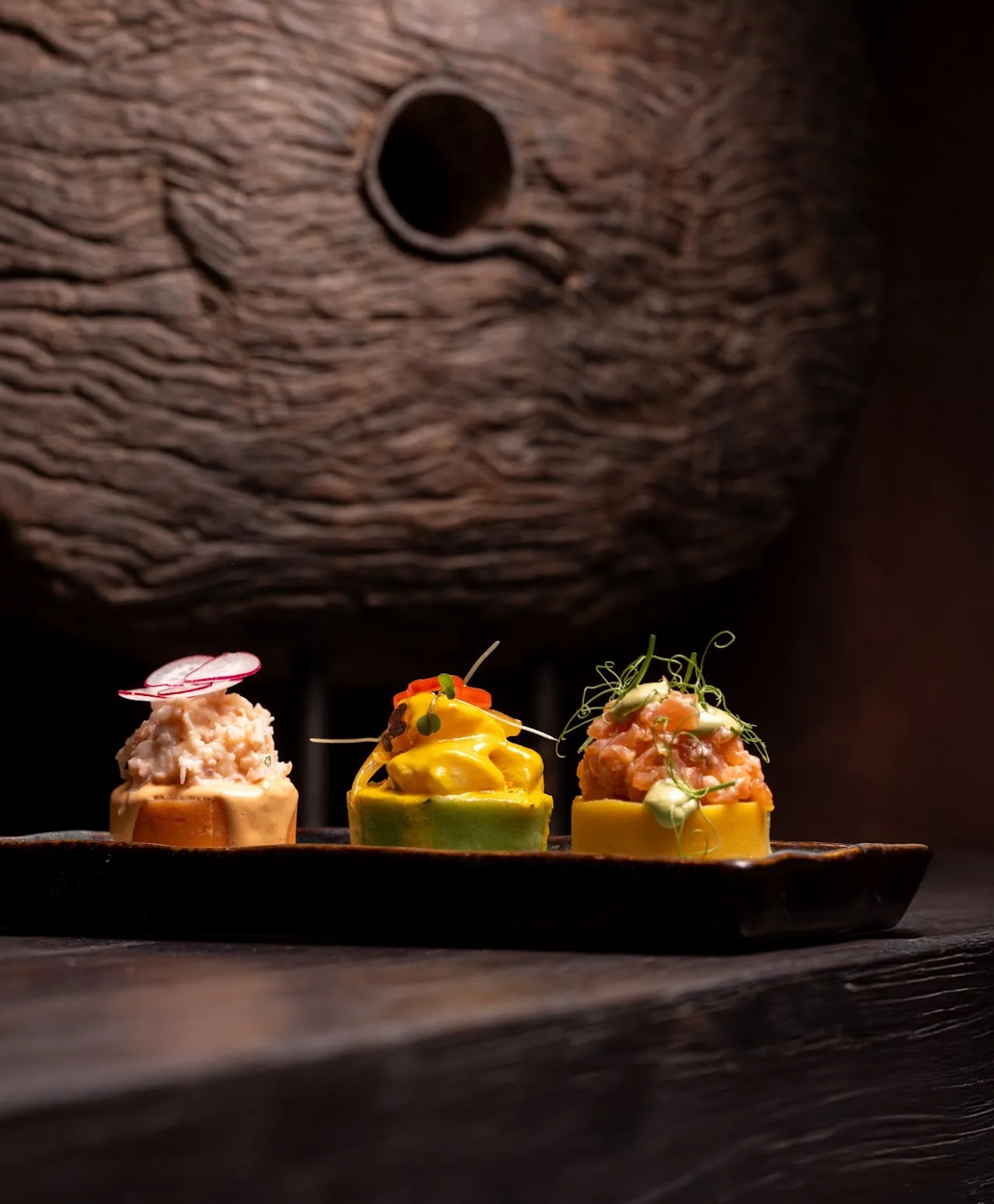 A wooden board with three causa Peruvian potato appetizers