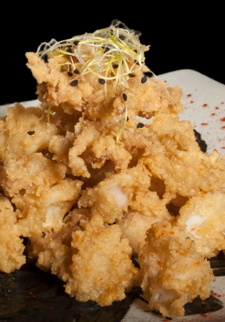 A pile of crisp fried seafood pieces topped with fine sprouts on a plate