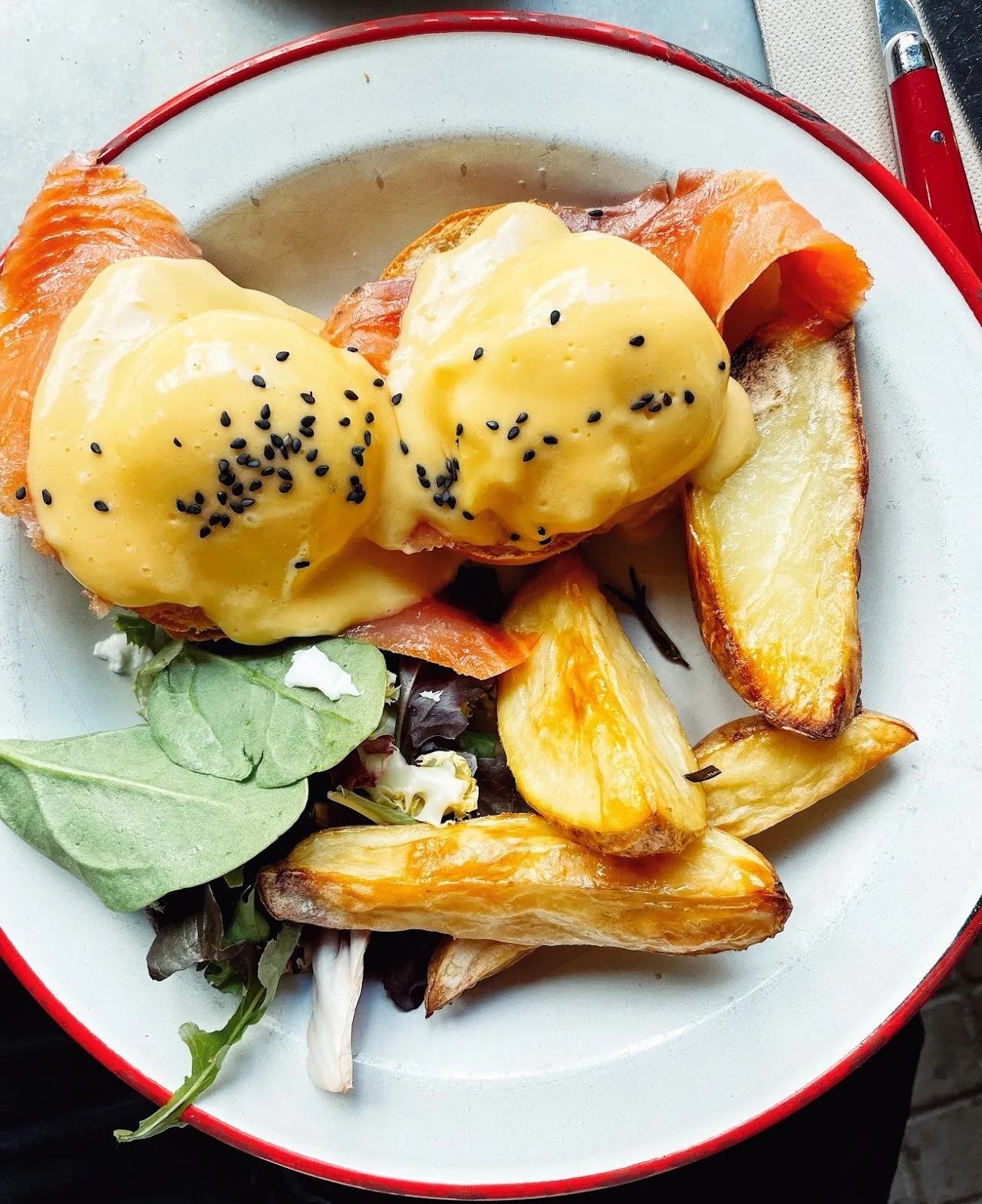 A plate of poached eggs with hollandaise sprinkled with black sesame, beside roasted potatoes and salad leaves