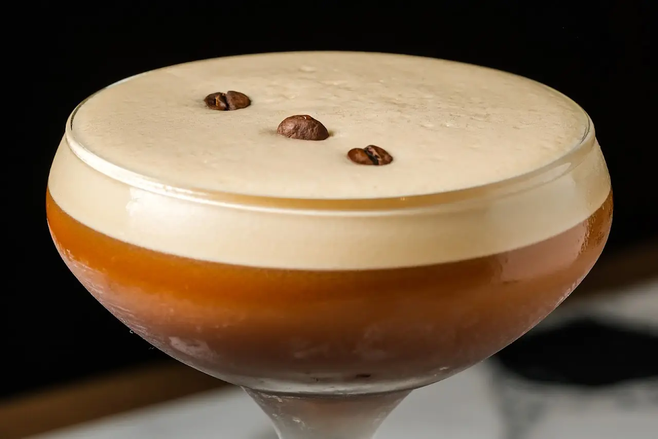 An espresso martini in a coupe glass garnished with three coffee beans.