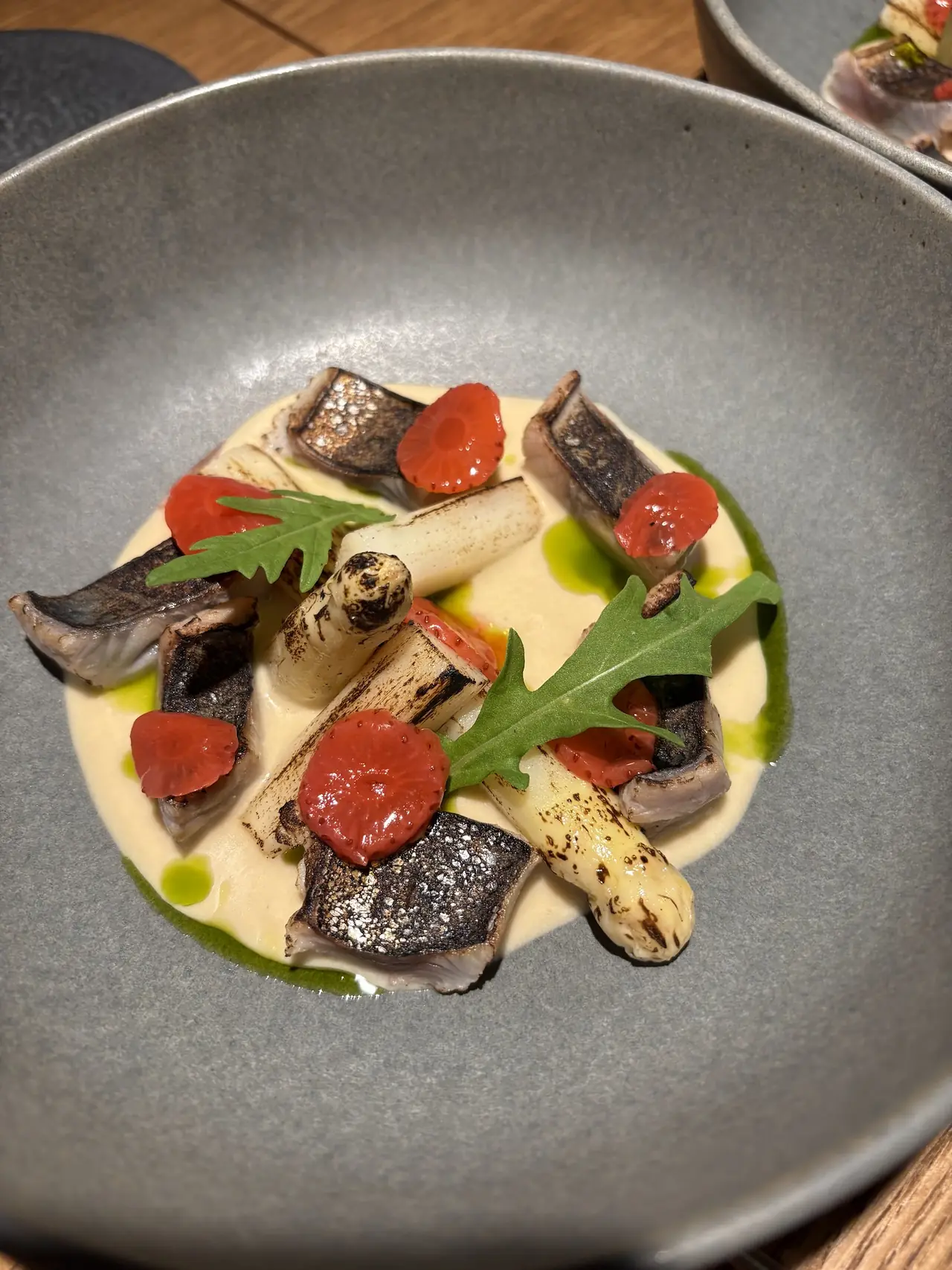Charred fish pieces and grilled white asparagus over a cream sauce, with cherry tomatoes and arugula
