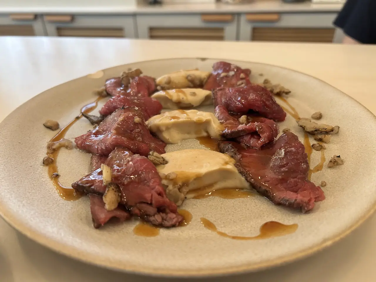 Sliced beef arranged around cream quenelles with jus and crushed nuts on a plate