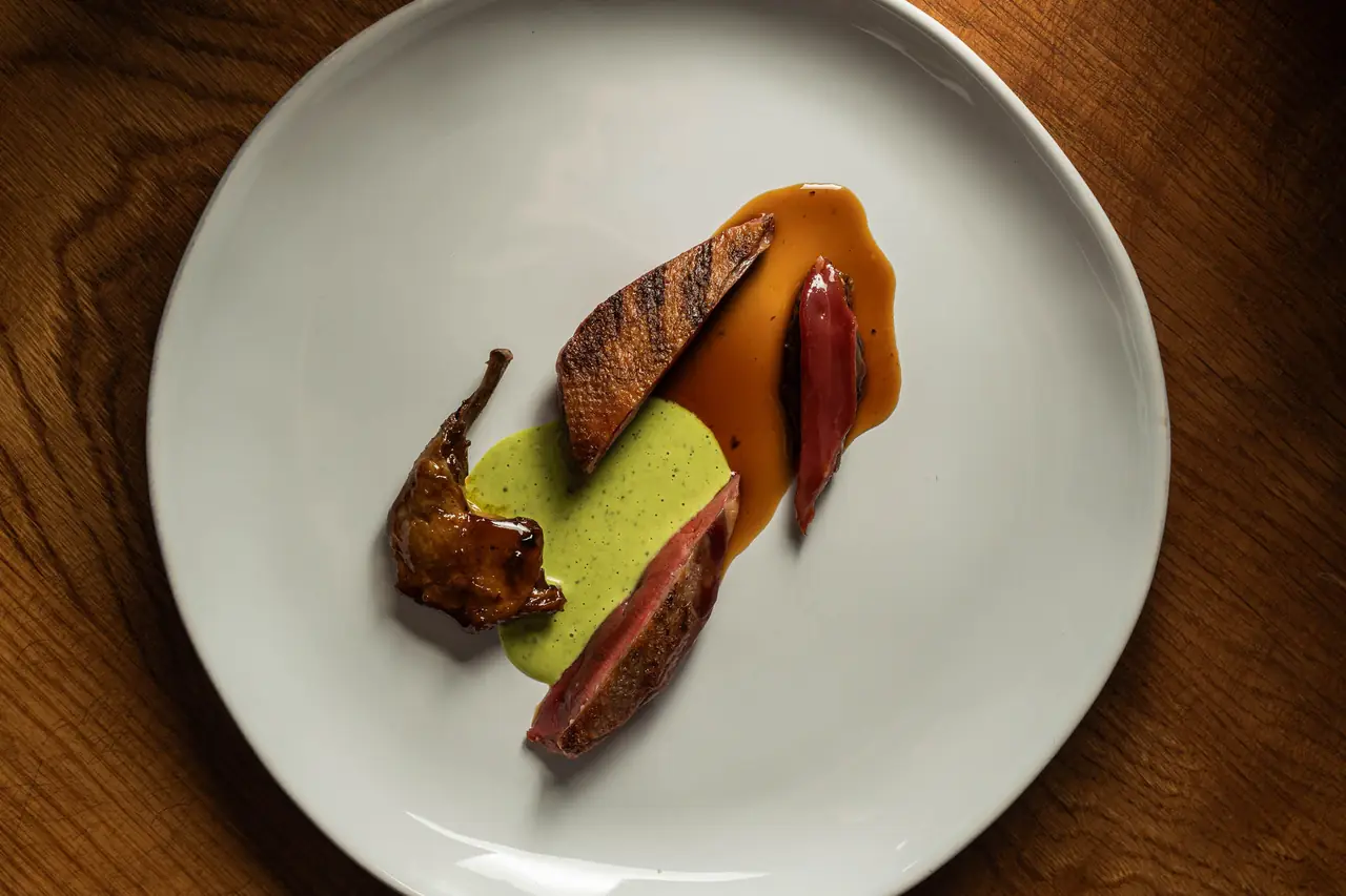 Plated grilled meat with a bright green herb sauce and glossy jus on a white plate at Agreste Mar