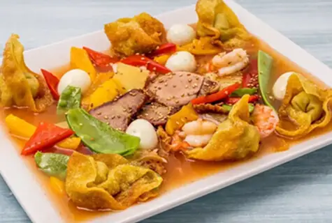 Fried wontons with shrimp, sliced pork, quail eggs and peppers in a light sauce on a white plate