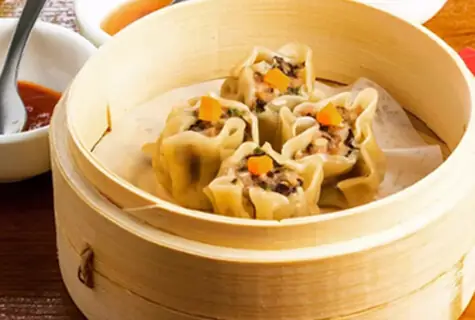 Steamed pork siu mai dumplings topped with diced carrot in a bamboo steamer