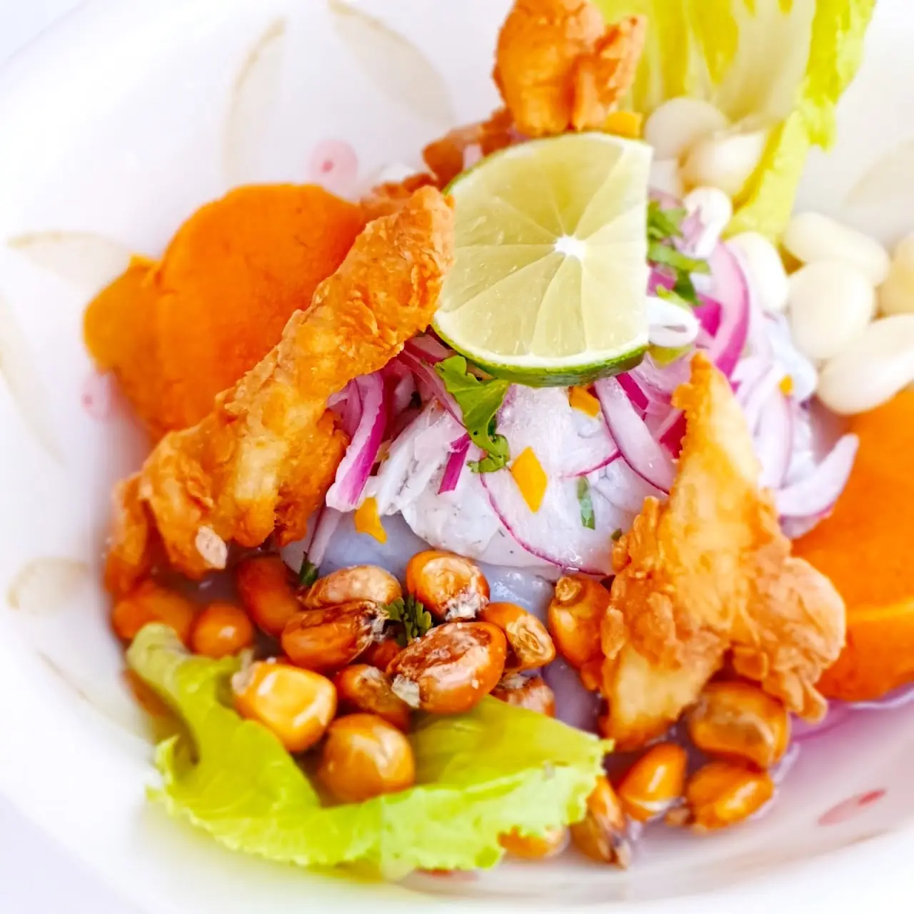 Battered shrimp served with lime wedges, sliced red onion, and corn kernels.