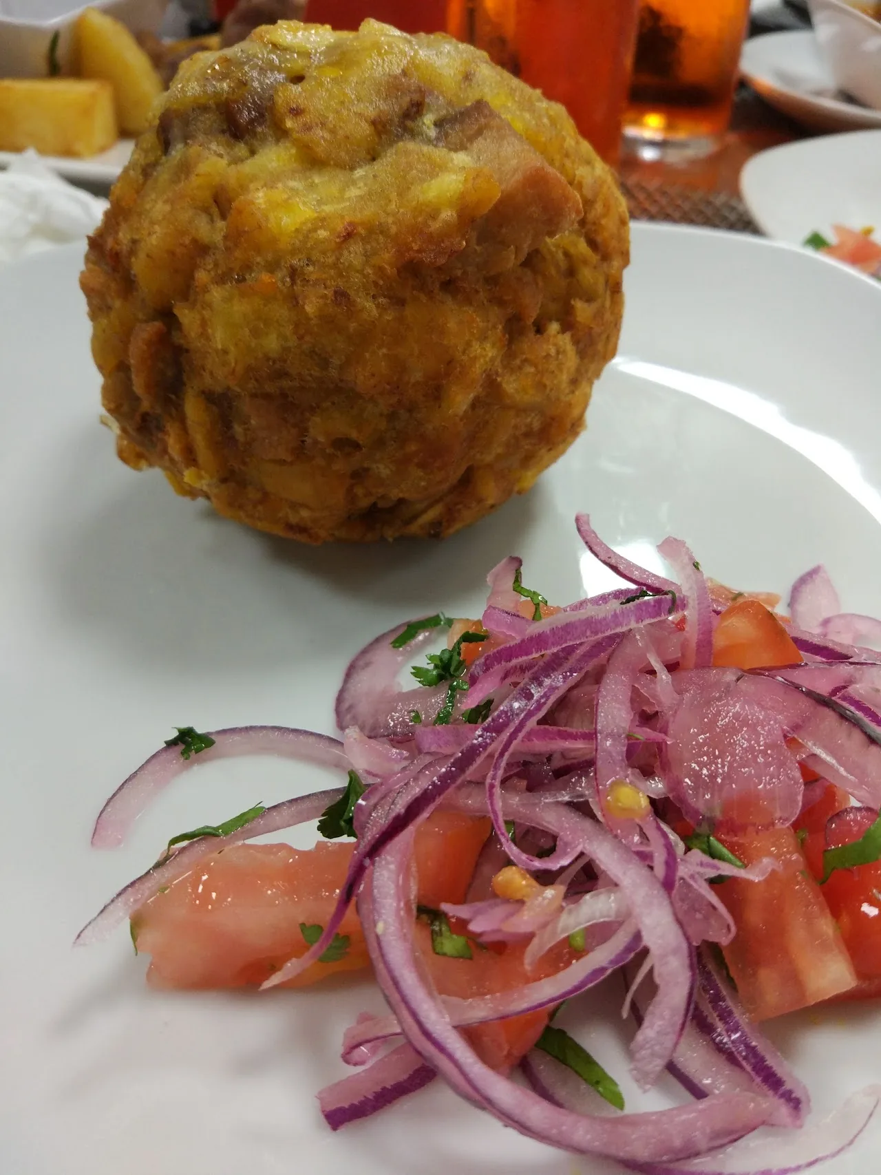 A fried meatball or empanada served with tomato and onion salad