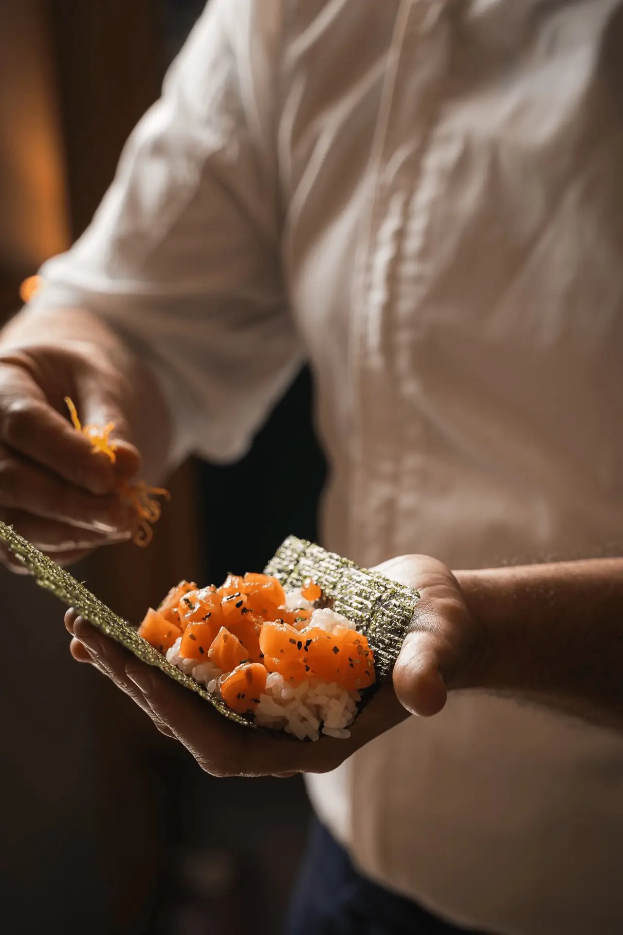 Chef assembling a salmon hand roll of nori, rice and diced salmon