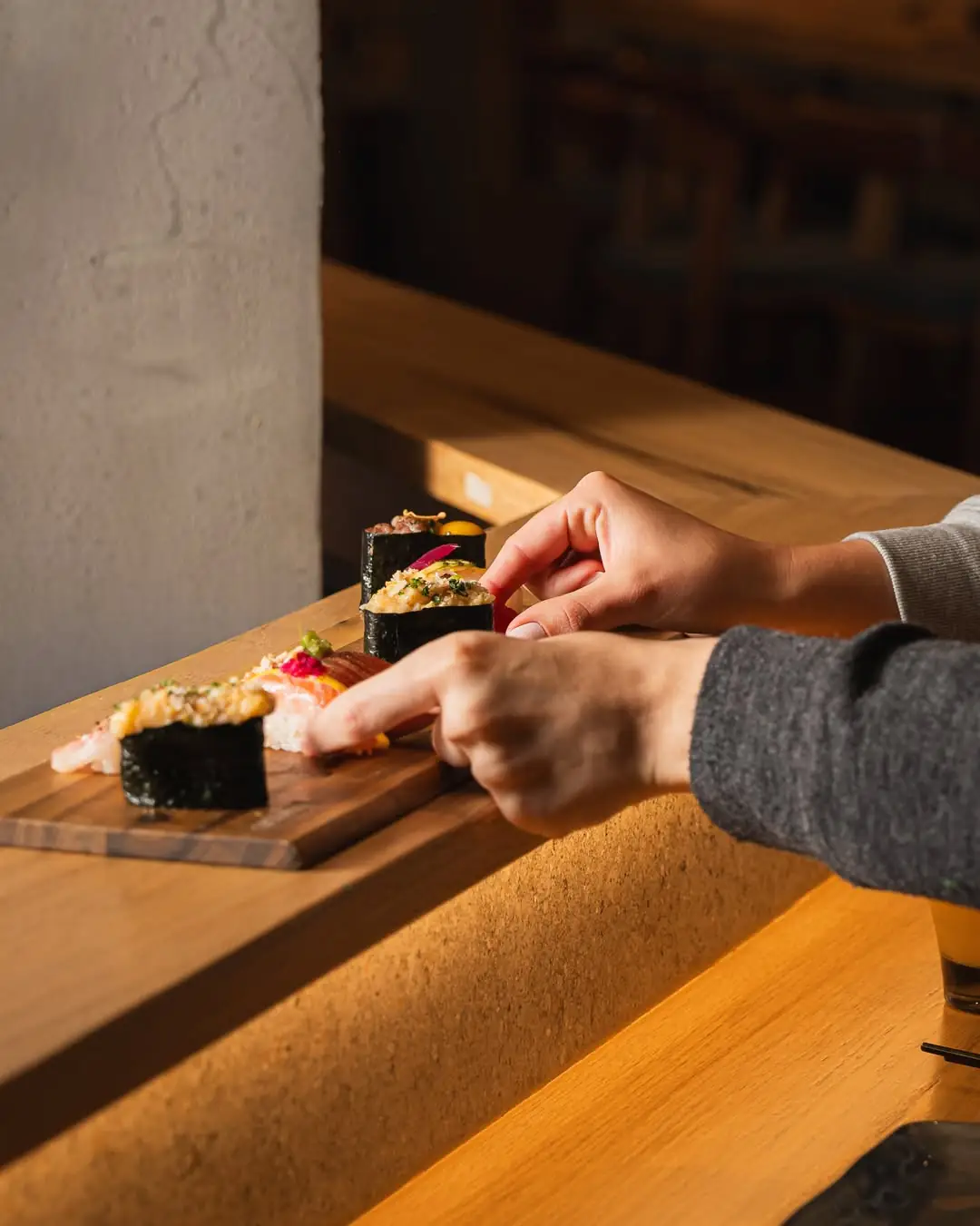 Nigiri and nori-wrapped sushi pieces arranged on a wooden serving board at the counter