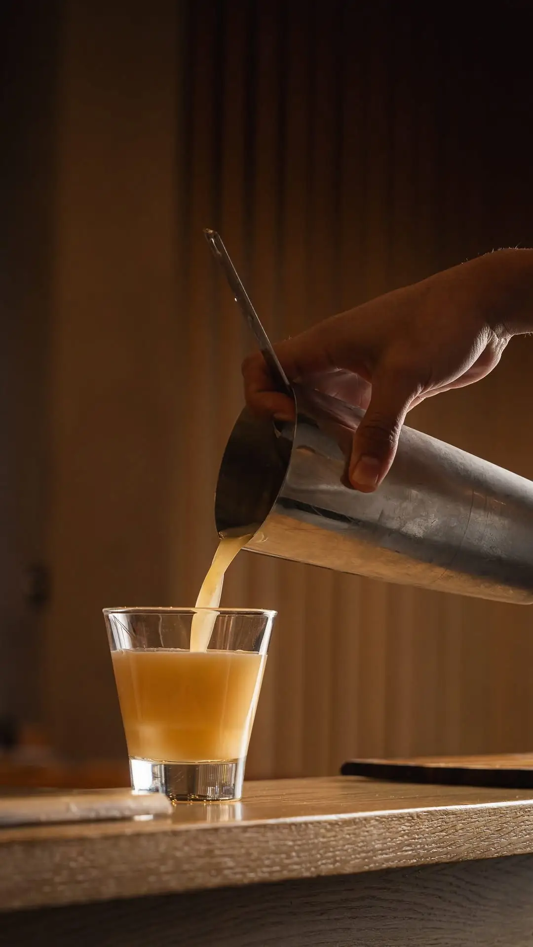 Bartender pouring a pale orange cocktail from a shaker into a rocks glass