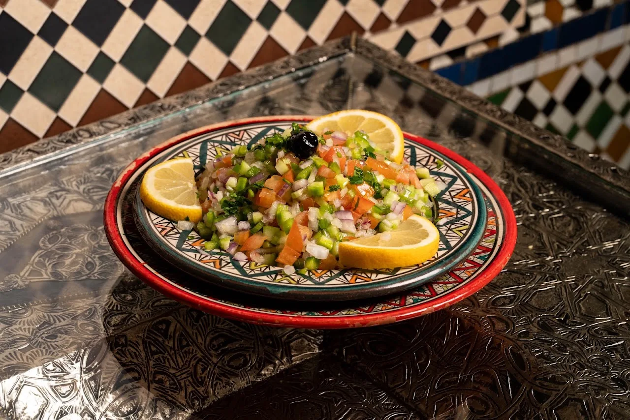 A salad with pomegranate seeds and tomatoes on a decorative plate