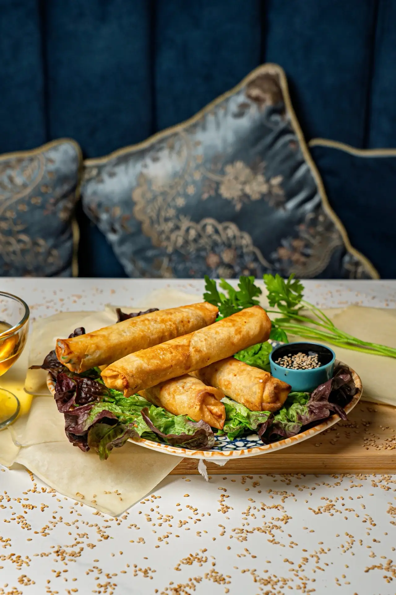 Fried spring rolls stacked on lettuce with a small dish of dark dipping sauce, on a patterned plate.