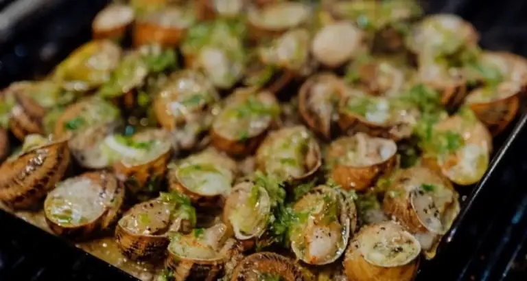 Grilled snails topped with green herb and garlic sauce on a metal tray, Alba Granados