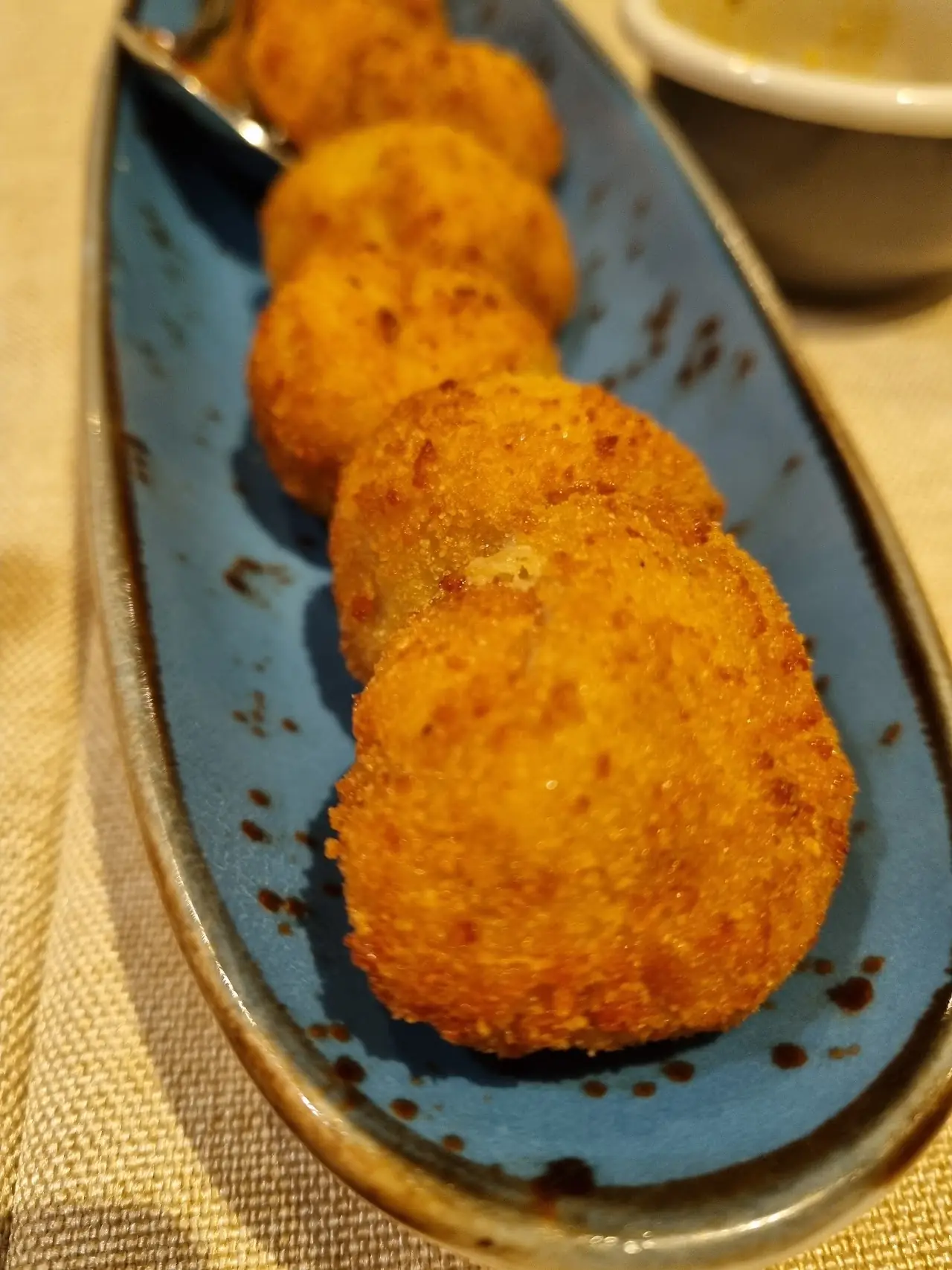 Four breaded and fried croquettes arranged on a dark oval plate.