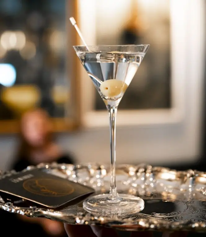 A martini garnished with an olive on a cocktail stick, served on an ornate silver tray