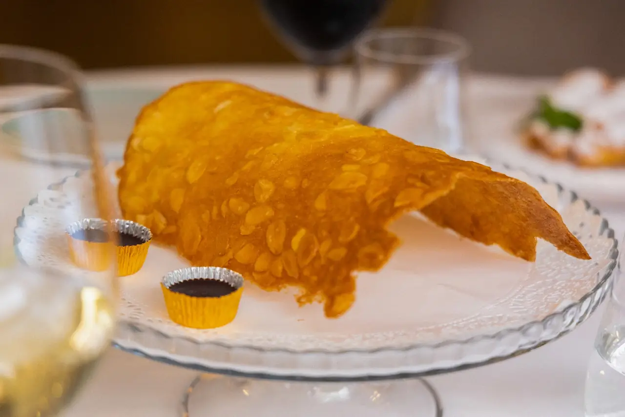 Large crispy sesame-crusted wafer served on a glass cake stand with two small pots of dark sauce