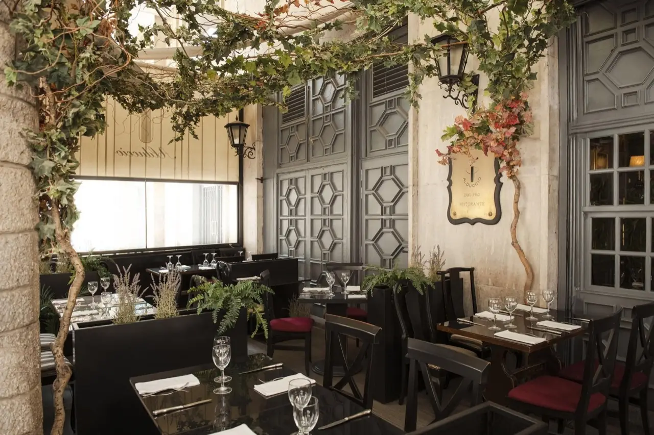 Alduccio dining terrace with set tables, black lacquered surfaces, ivy overhead and a brass restaurant plaque on the wall