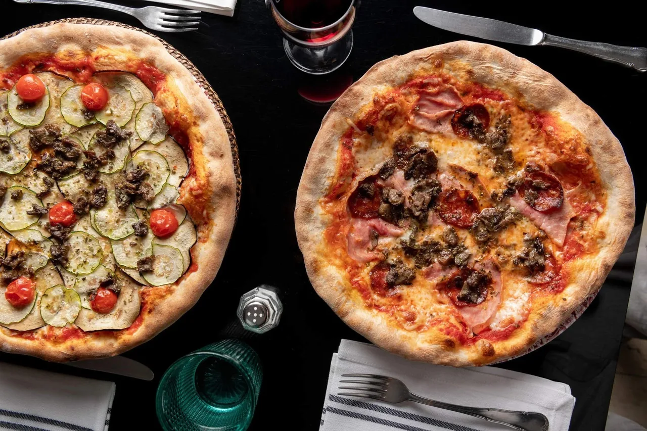 Two pizzas with toppings seen from above on a dark table