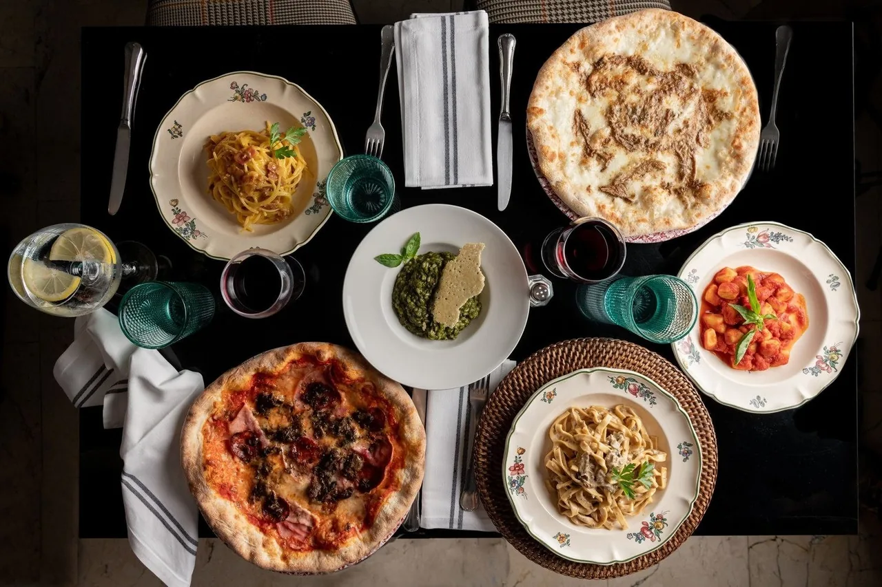 An overhead view of pizzas and pasta dishes on a dark table