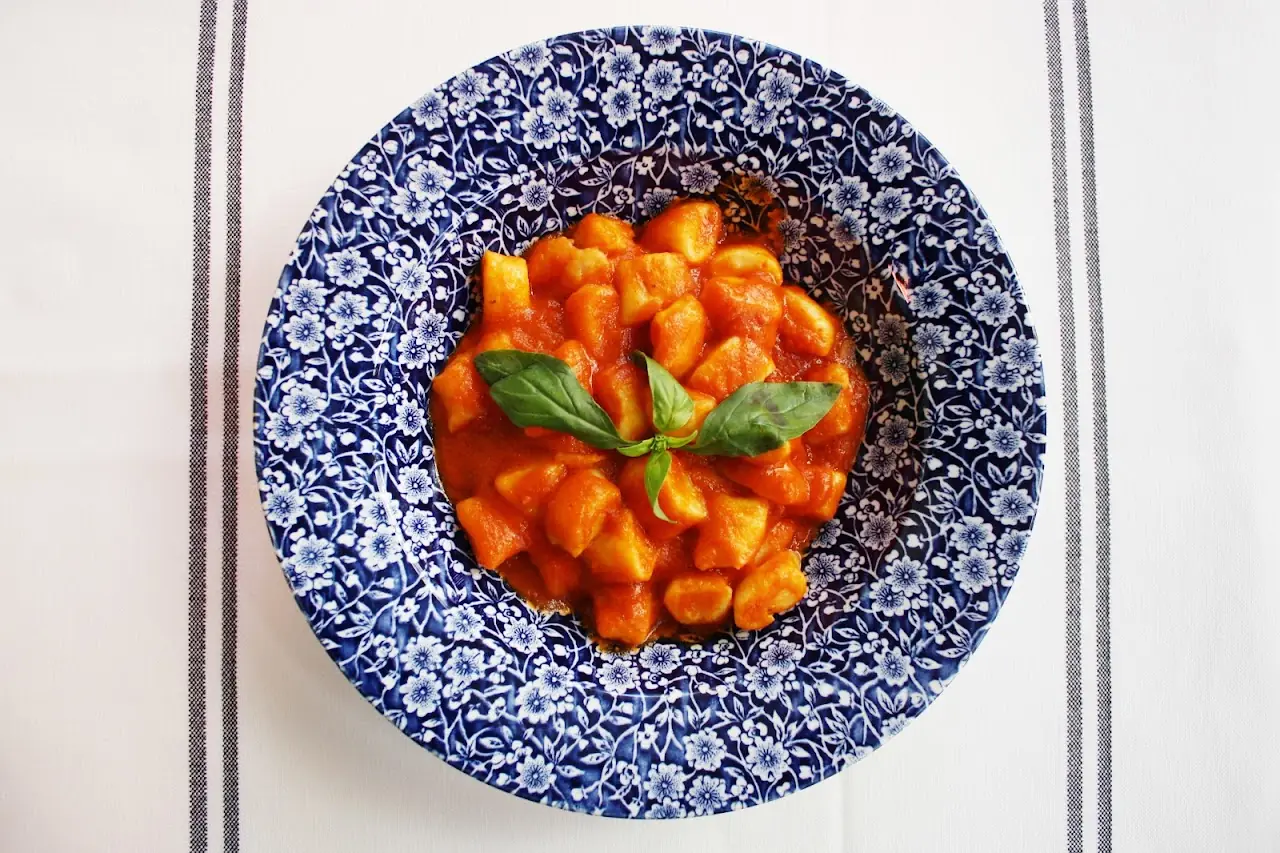 Gnocchi in tomato sauce with a basil leaf on a blue-patterned plate.
