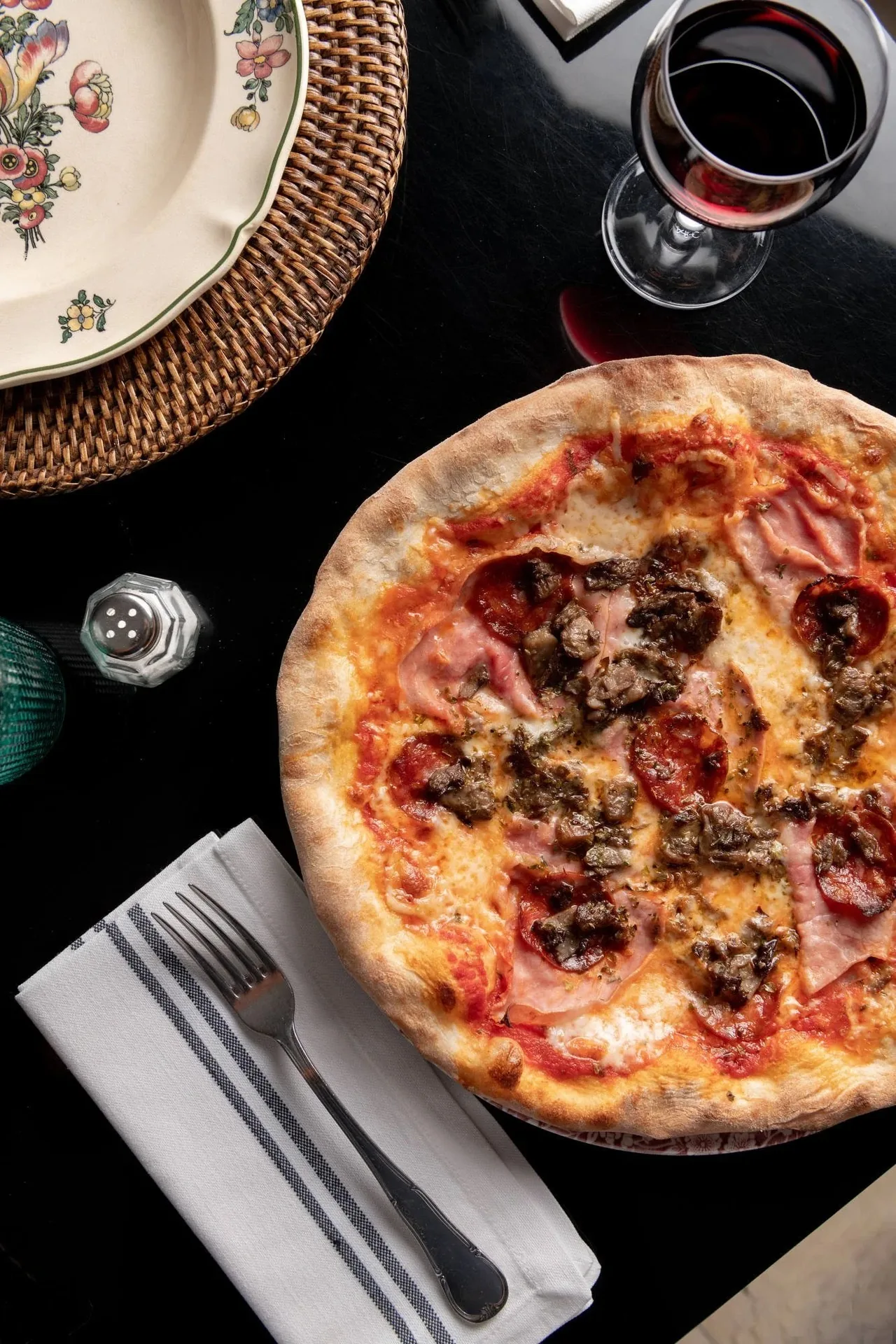 A pizza with ham and toppings seen from above on a plate on a dark table