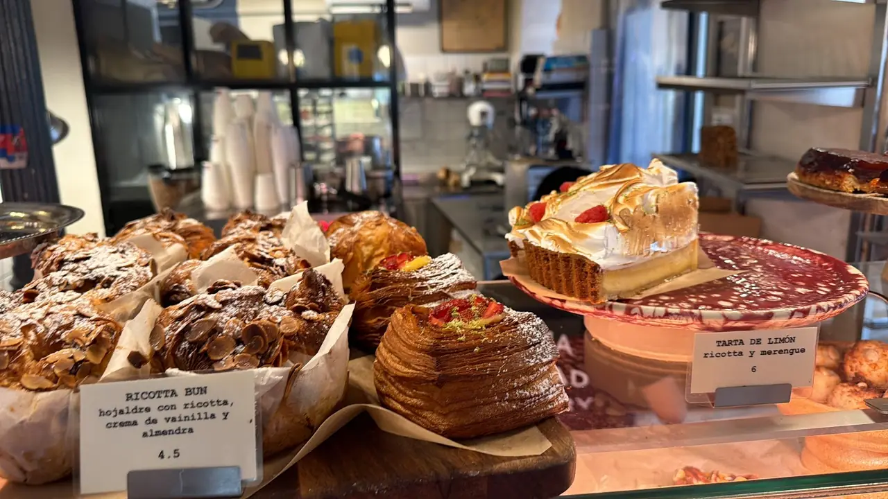 Display case of pastries including a ricotta bun and a lemon meringue tart with price cards